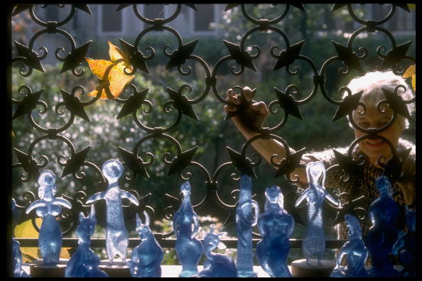 Peggy Guggenheim at her palazzo, peeking through an elaborate wrought iron fence, with glass figures designed by Picasso. Credit: David Lees/The LIFE Images Collection/Getty Images